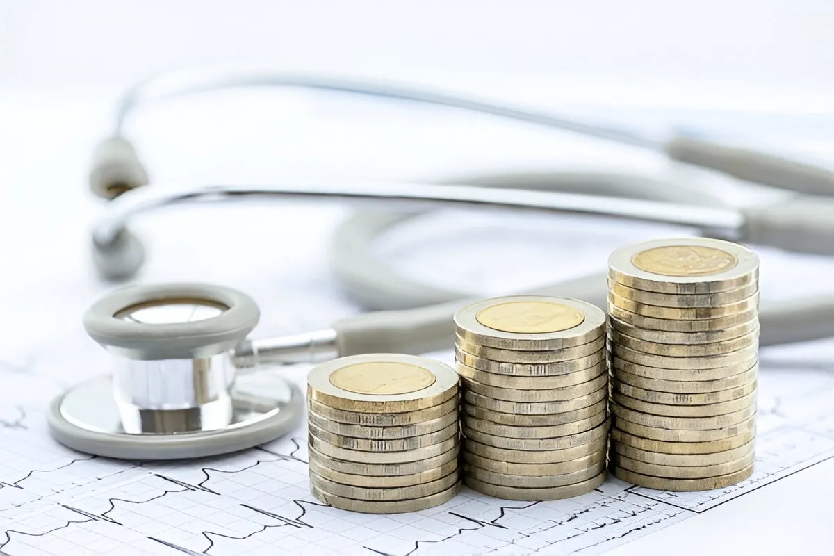 Stacks of coins next to a stethoscope on a medical chart, symbolizing hospital billing services and healthcare costs..