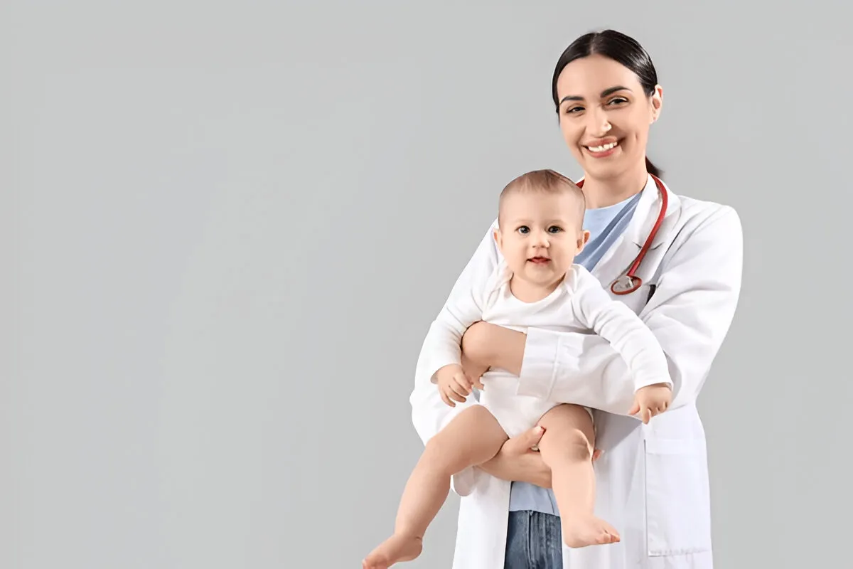 Pediatric doctor smiling while holding a baby during a checkup visit.
